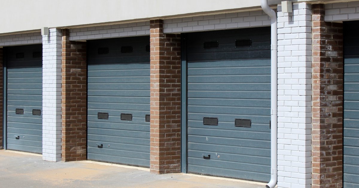 The exterior of a white and brown brick building. The building has four blue overhead doors separated by brick columns.