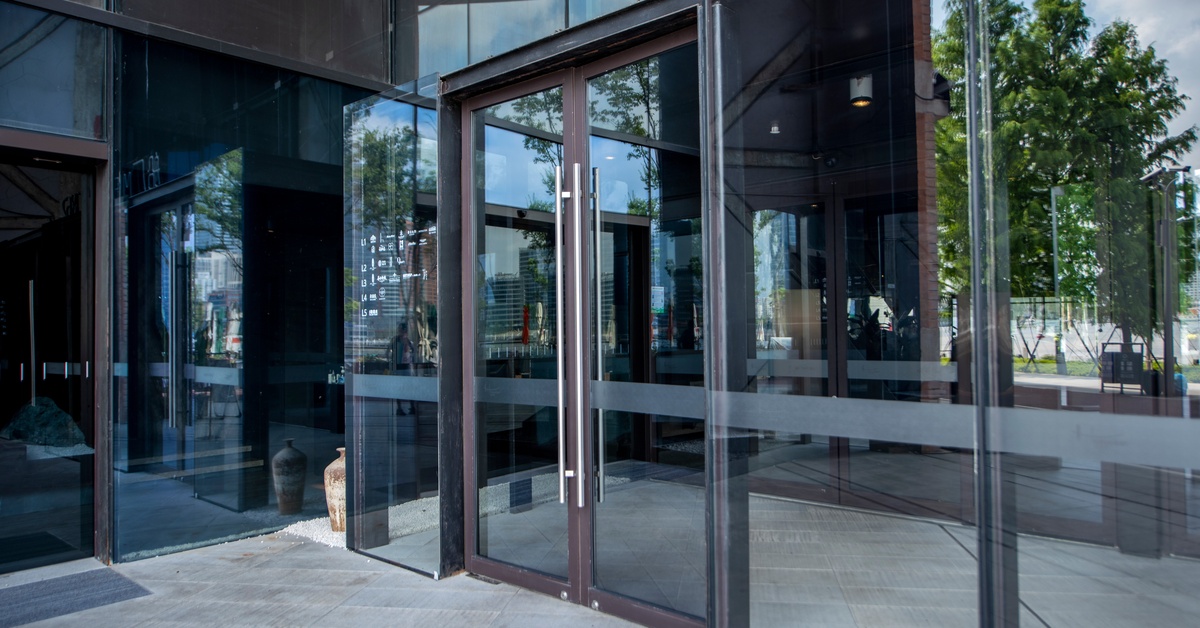 The exterior entrance of a commercial building with double glass doors and windows surrounding the doors.