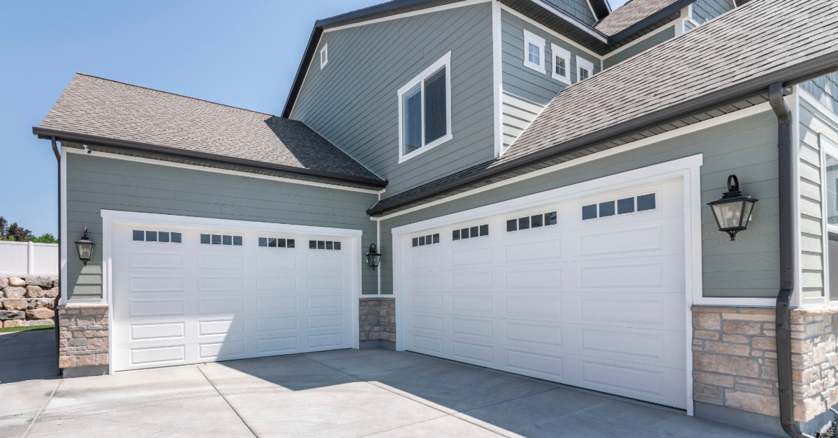 A house with two white garage doors that have small windows. The concrete driveway leads up to the house and the doors.