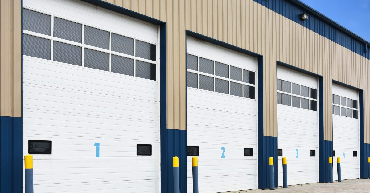 A commercial building with large white roll-up doors. Each door is numbered and has a variety of windows.